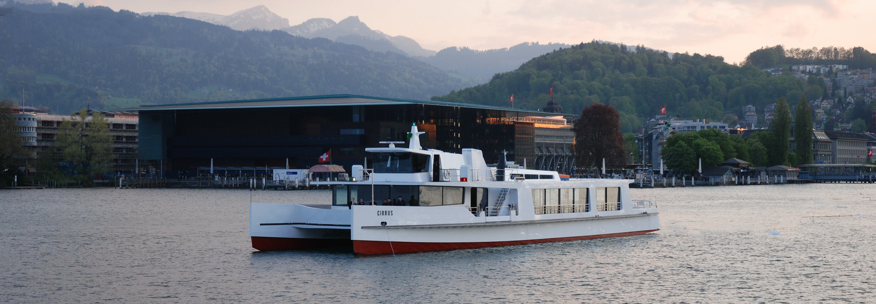 Par temps nuageux, le bateau à moteur Cirrus navigue dans le bassin du lac de Lucerne, à l'arrière-plan on aperçoit le KKL. 